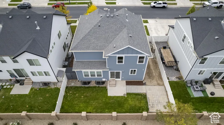 Two-story home with a multi-textured exterior, asphalt shingle roof, rear concrete patio, fully enclosed perimeter fencing, and a grass lawn