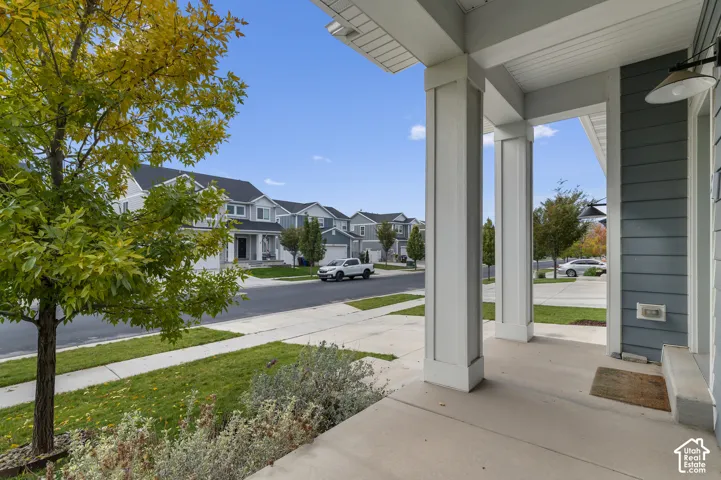 Covered front porch featuring concrete flooring, square columns, and exterior wall-mounted lighting