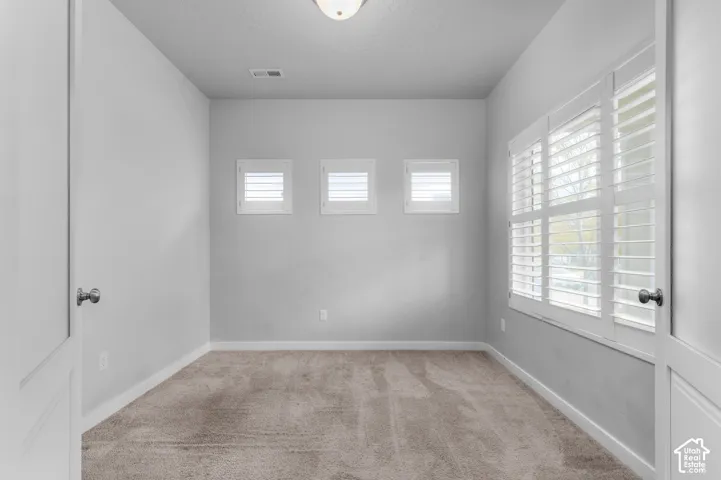 Interior room featuring wall-to-wall carpeting, three square windows with white plantation shutters, and a large multi-pane window assembly also equipped with white plantation shutters