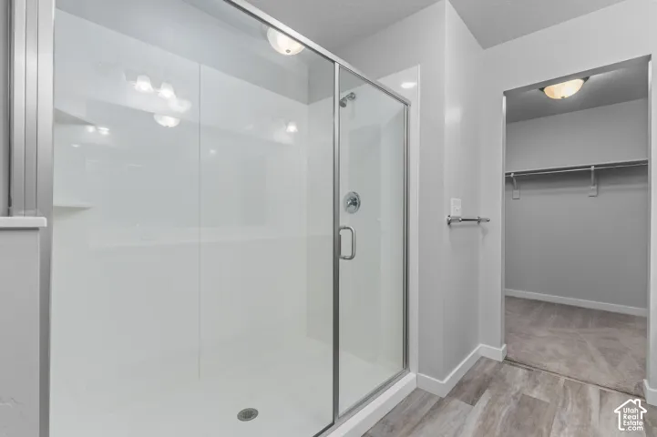 Walk-in shower with a glass enclosure, integrated shelving, and metal hardware, featuring wood-finish flooring and a walk-in storage area with a built-in rod