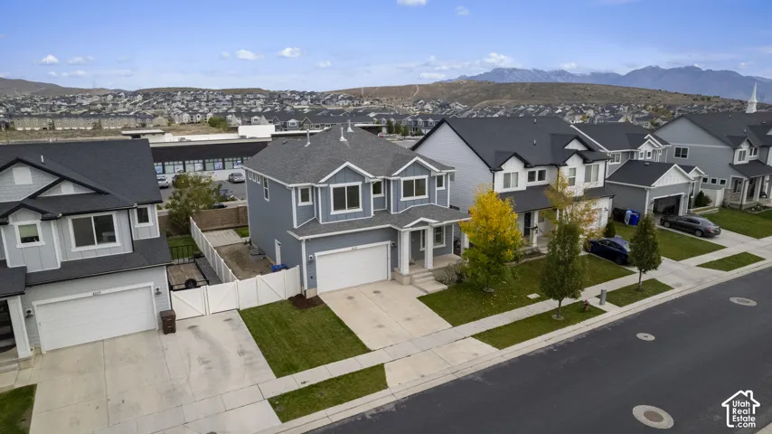 Two-story residence featuring a multi-gabled roofline, lap siding exterior, double-car garage, concrete driveway, and white vinyl privacy fencing against a mountain backdrop
