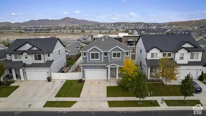 Two-story residence featuring a gray exterior finish, steep gable roofline, attached multi-car garage, concrete driveway, and mountain backdrop