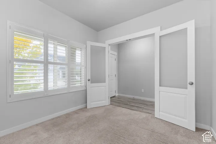 Interior space featuring white-trimmed glass-paneled double doors, interior plantation shutters, neutral-toned wall-to-wall carpeting, and wood-finish flooring