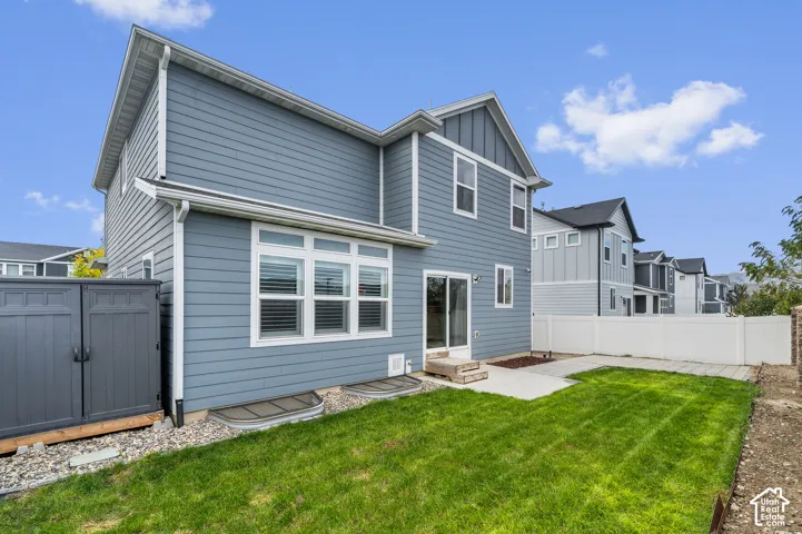 Blue horizontal lap siding exterior featuring vertical board-and-batten accents, concrete patio, white vinyl perimeter fencing, and a manicured lawn