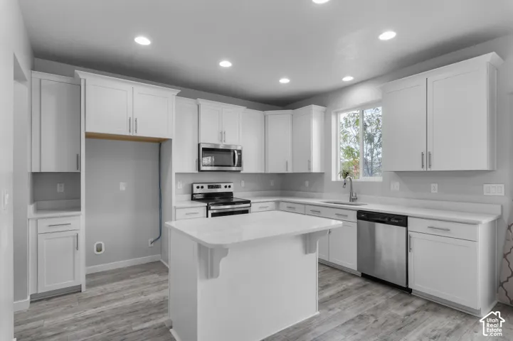 Kitchen featuring white shaker-style cabinetry, a central island with a solid-surface countertop, stainless steel appliances, recessed lighting, and wood-finish flooring