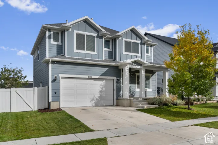 Two-story residence featuring blue horizontal and vertical board-and-batten siding, a covered front porch with square columns, an attached two-car garage, and white vinyl perimeter fencing