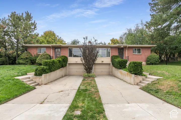 Brick facade exterior featuring two attached garages, a concrete driveway, and tiered landscaping