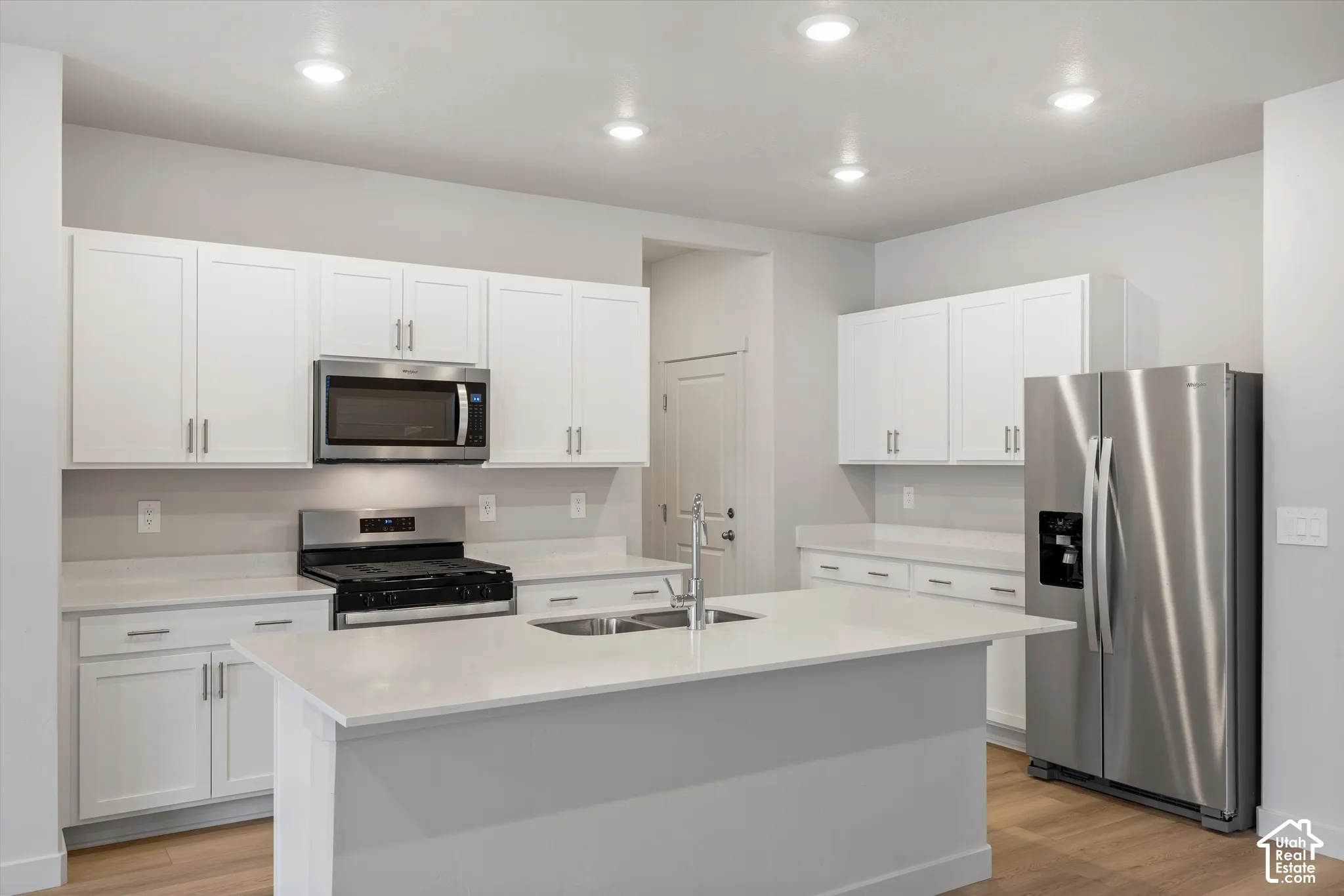 Kitchen featuring white cabinetry, solid-surface countertops, center island with integrated sink, stainless steel appliances, and recessed lighting