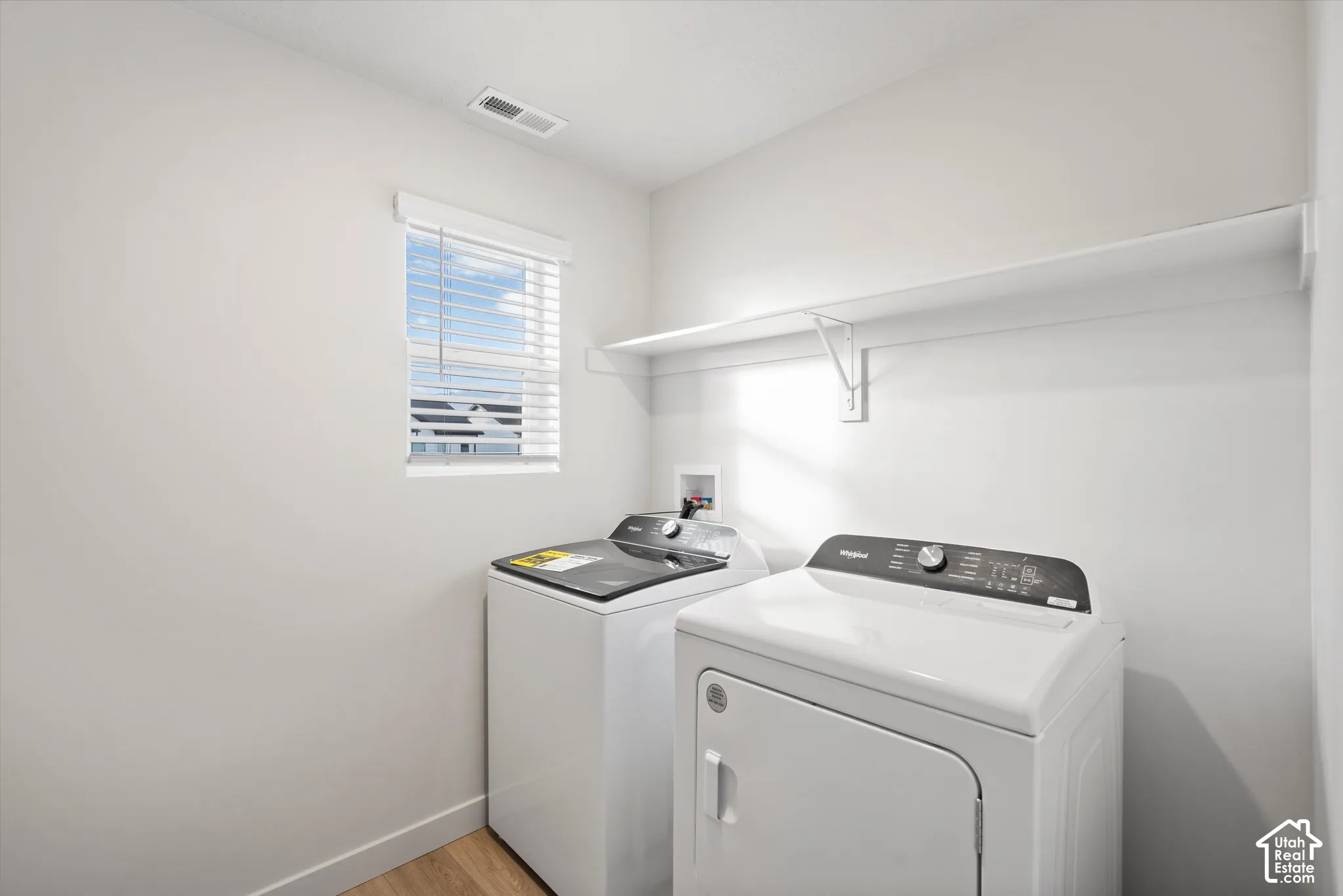 Laundry area featuring wood-finish flooring, a window with horizontal blinds, and built-in wall shelving