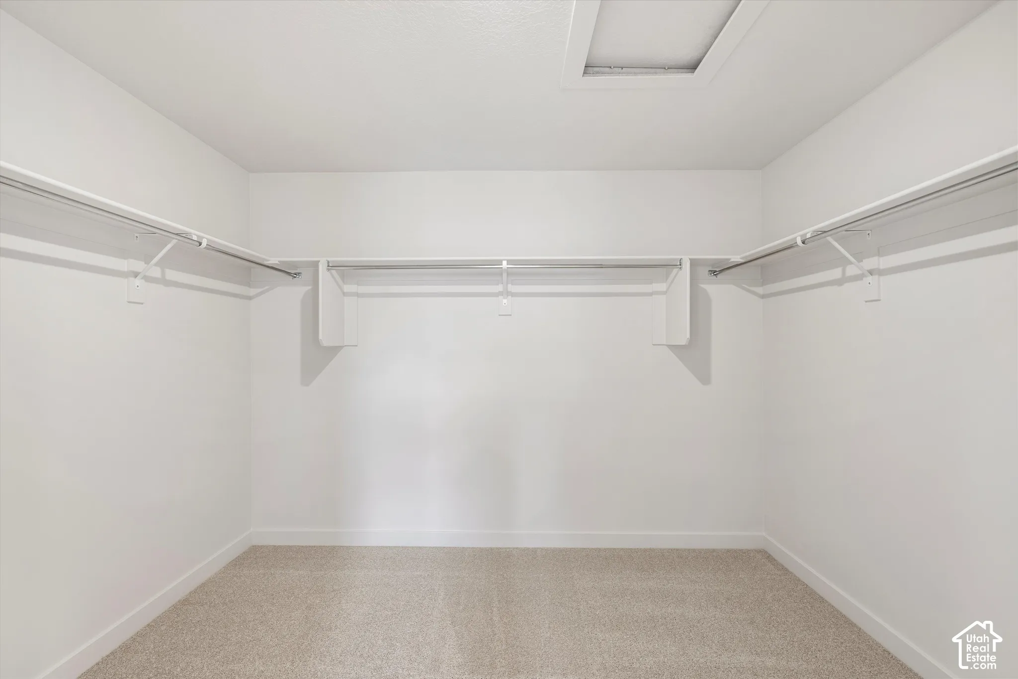 Walk-in closet featuring neutral carpeting and integrated tiered shelving with metal garment rods