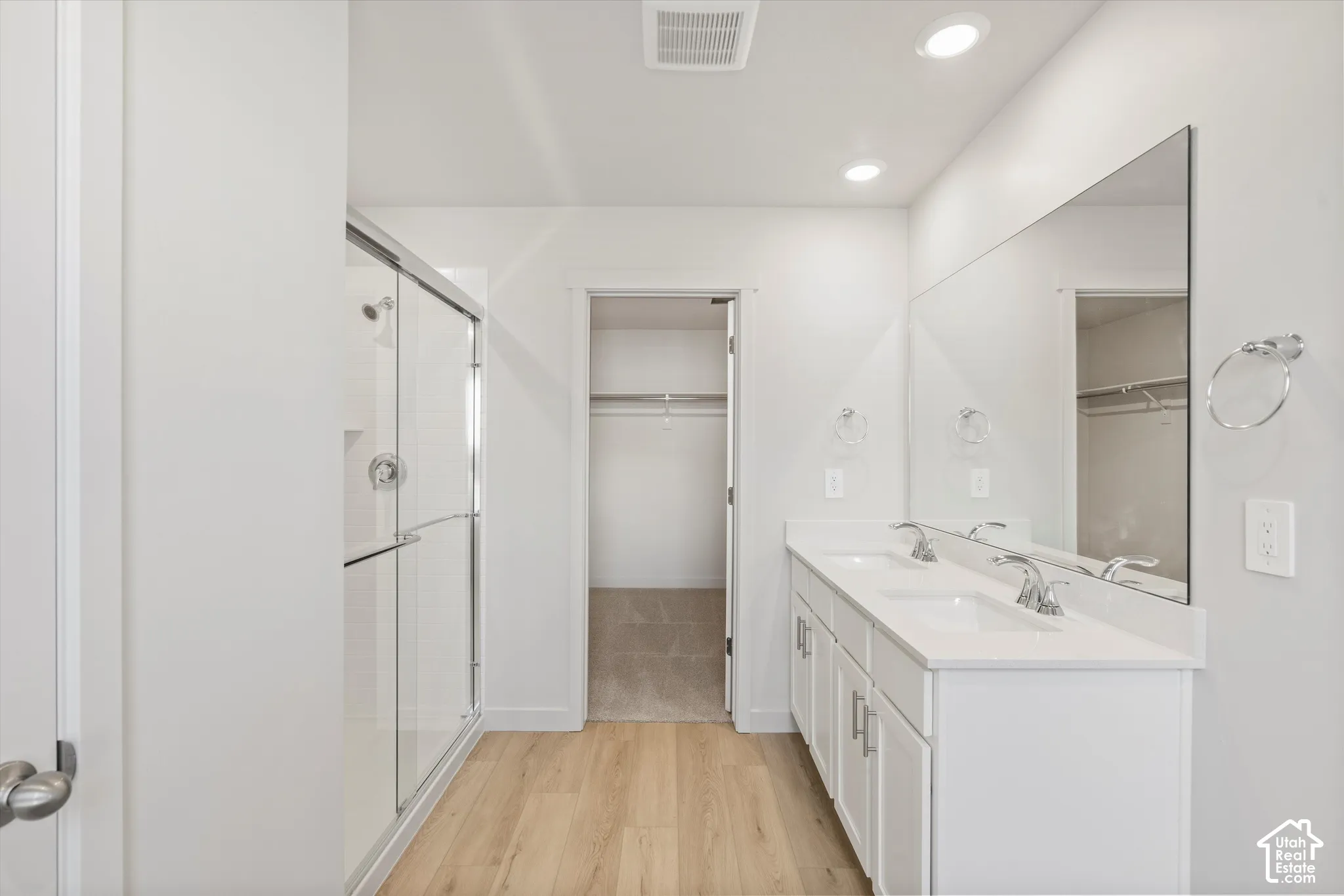 Double-vanity cabinet with stone-finish countertop, full-width wall mirror, glass-enclosed shower, and wood-finish flooring