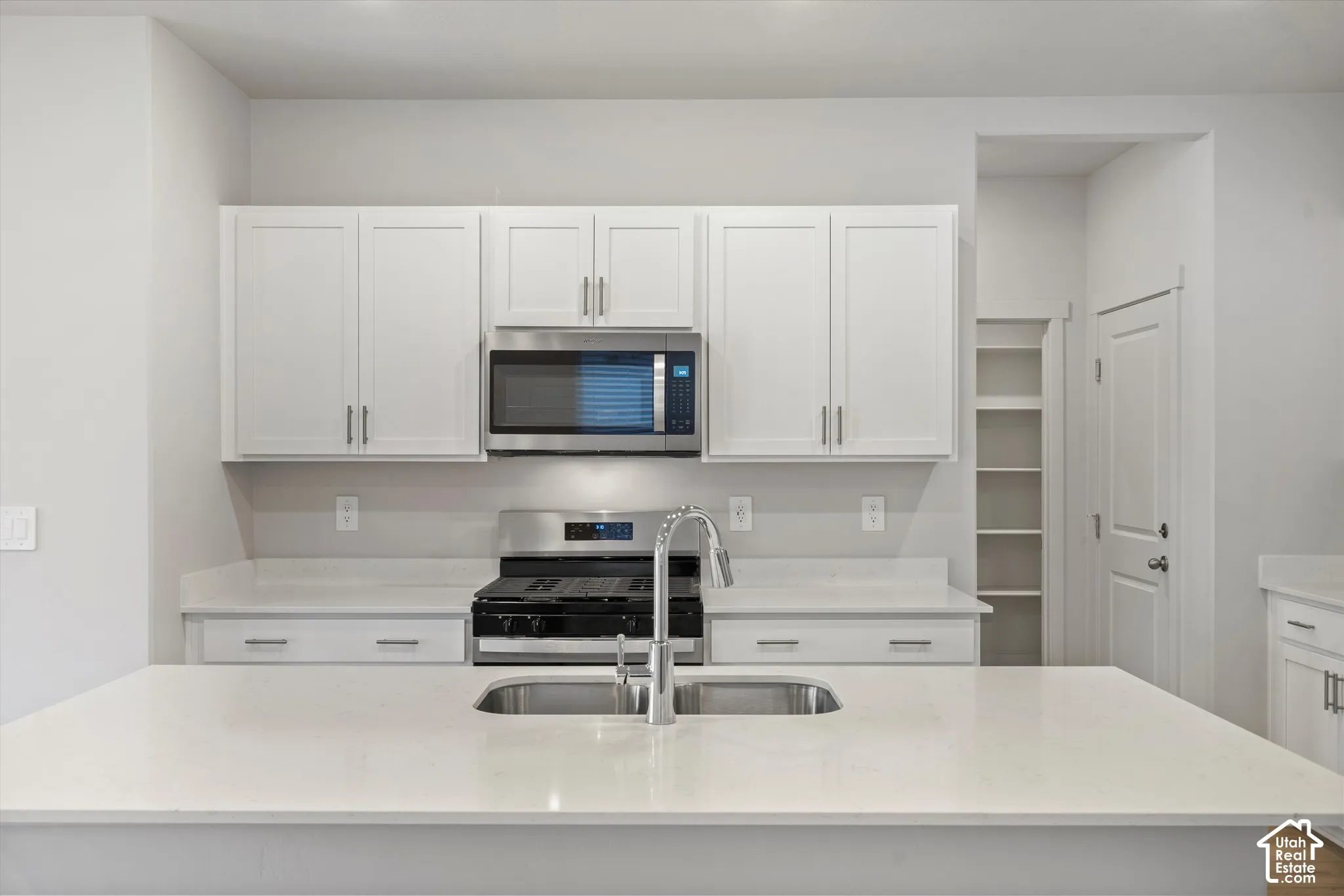 Kitchen featuring white shaker-style cabinetry, a stone-surface island with an undermount dual-basin stainless steel sink, a stainless steel gas range, and a built-in pantry