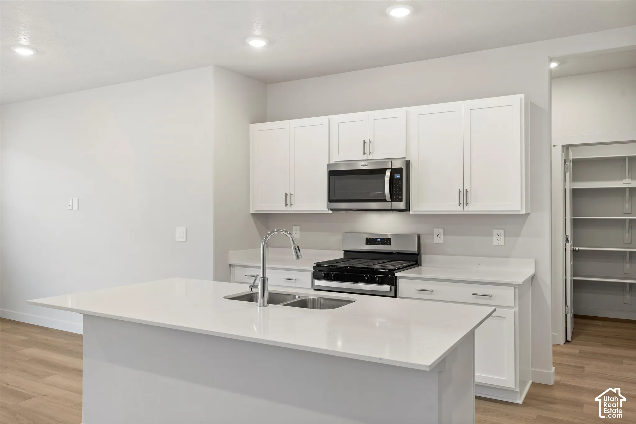 Kitchen featuring white cabinetry, quartz countertops, stainless steel appliances, a central island with an undermount sink, and a walk-in pantry