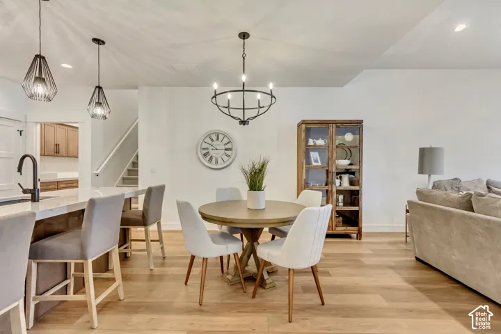 Open-concept interior featuring light wood-finish flooring, a kitchen island with stone-surface countertop, matte black fixtures, industrial-style geometric pendant lighting, and a circular iron chandelier