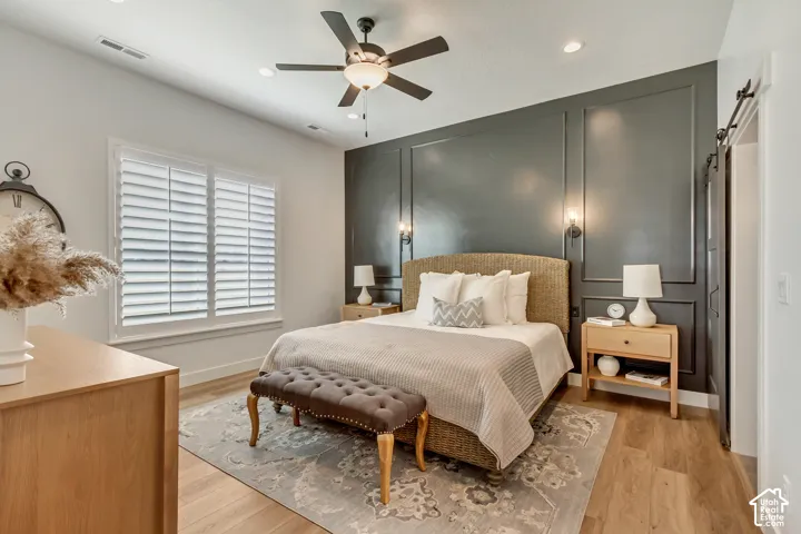 Bedroom featuring a dark-toned paneled accent wall, recessed lighting, ceiling fan with integrated lighting, plantation shutters, and wood-finish flooring