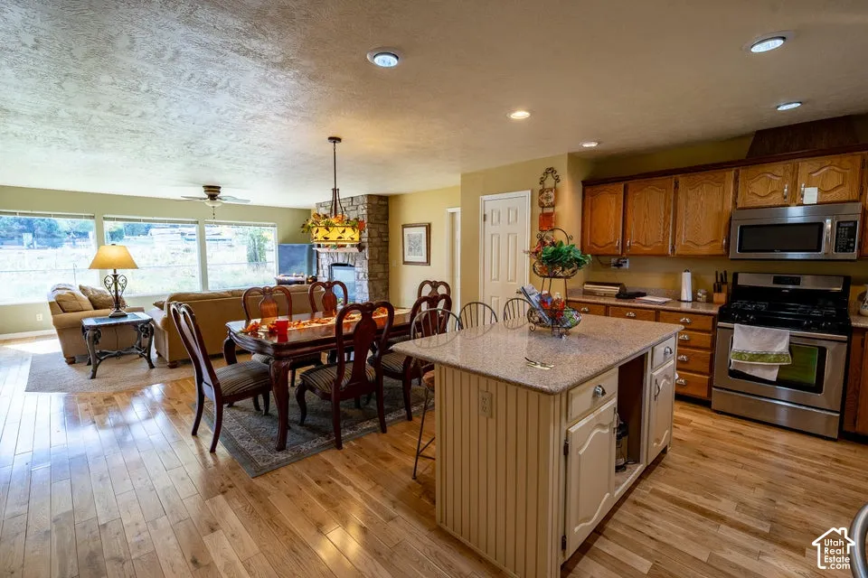 Kitchen featuring wood cabinetry, stainless steel appliances, a stone-surround fireplace, a center island with countertop seating, and wood-finish flooring