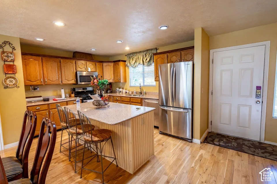 Kitchen featuring wood cabinetry, solid-surface countertops, central island, stainless steel appliances, and wood-finish flooring