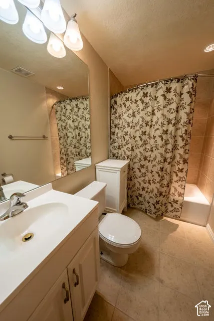 Bathroom featuring a white vanity with an integrated basin, wall-mounted mirror, multi-bulb lighting fixture, tiled tub surround, and ceramic tile flooring