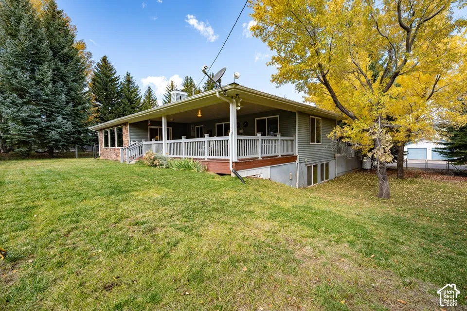 Exterior featuring a covered wrap-around deck, horizontal siding, brick masonry accents, and an expansive lawn with mature trees