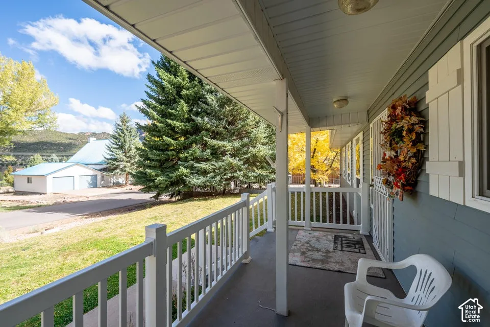 Covered front porch featuring white railing, vinyl siding, shutter accents, and mountain scenery