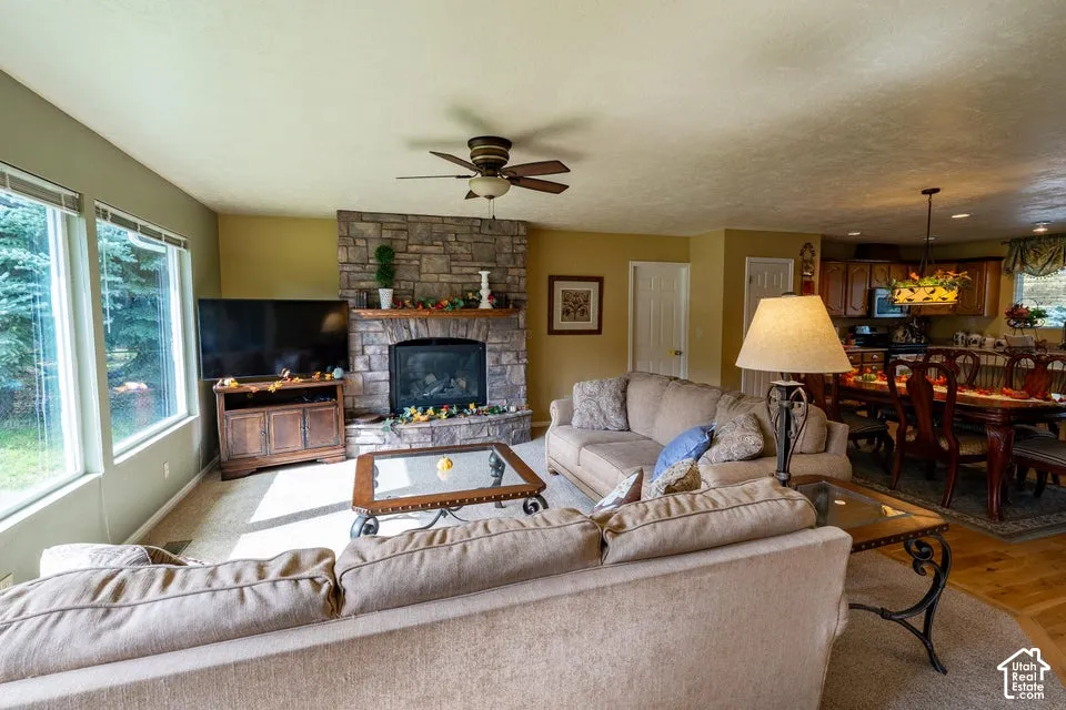 Floor-to-ceiling stone fireplace, large picture windows, wood-finish flooring, and recessed ceiling fan