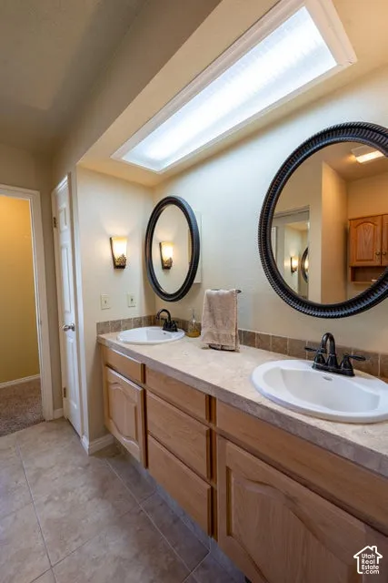 Dual-sink vanity with stone-texture countertop, wood cabinetry, recessed ceiling lighting, and two oval wall-mounted mirrors
