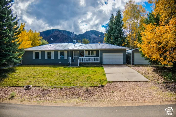 Single-story residence featuring a metal roof, white porch railing, attached garage, detached storage structure, and mountain backdrop