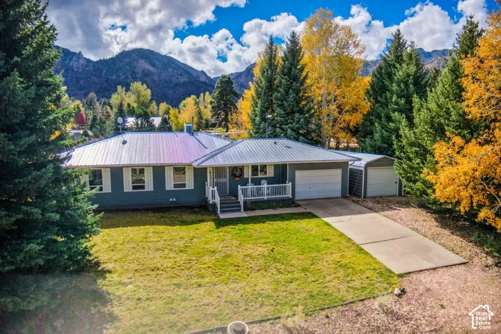 Single-story residence featuring a metal roof, attached garage, covered front porch with white railing, and exterior siding, set against a mountainous backdrop