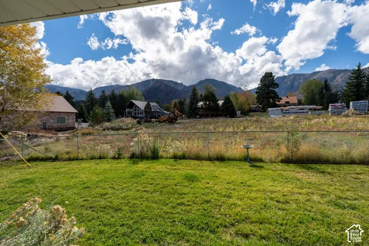 Fenced backyard featuring a manicured lawn, established landscaping, and a backdrop of mountain peaks