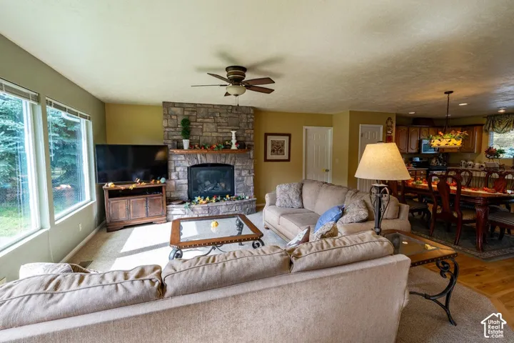 Floor-to-ceiling stone fireplace, large picture windows, wood-finish flooring, and recessed ceiling fan