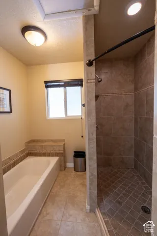 Bathroom featuring a deep soaking tub with a tiled surround, a separate walk-in shower with stone-finish tiling and patterned floor accents, and a window with a roller shade