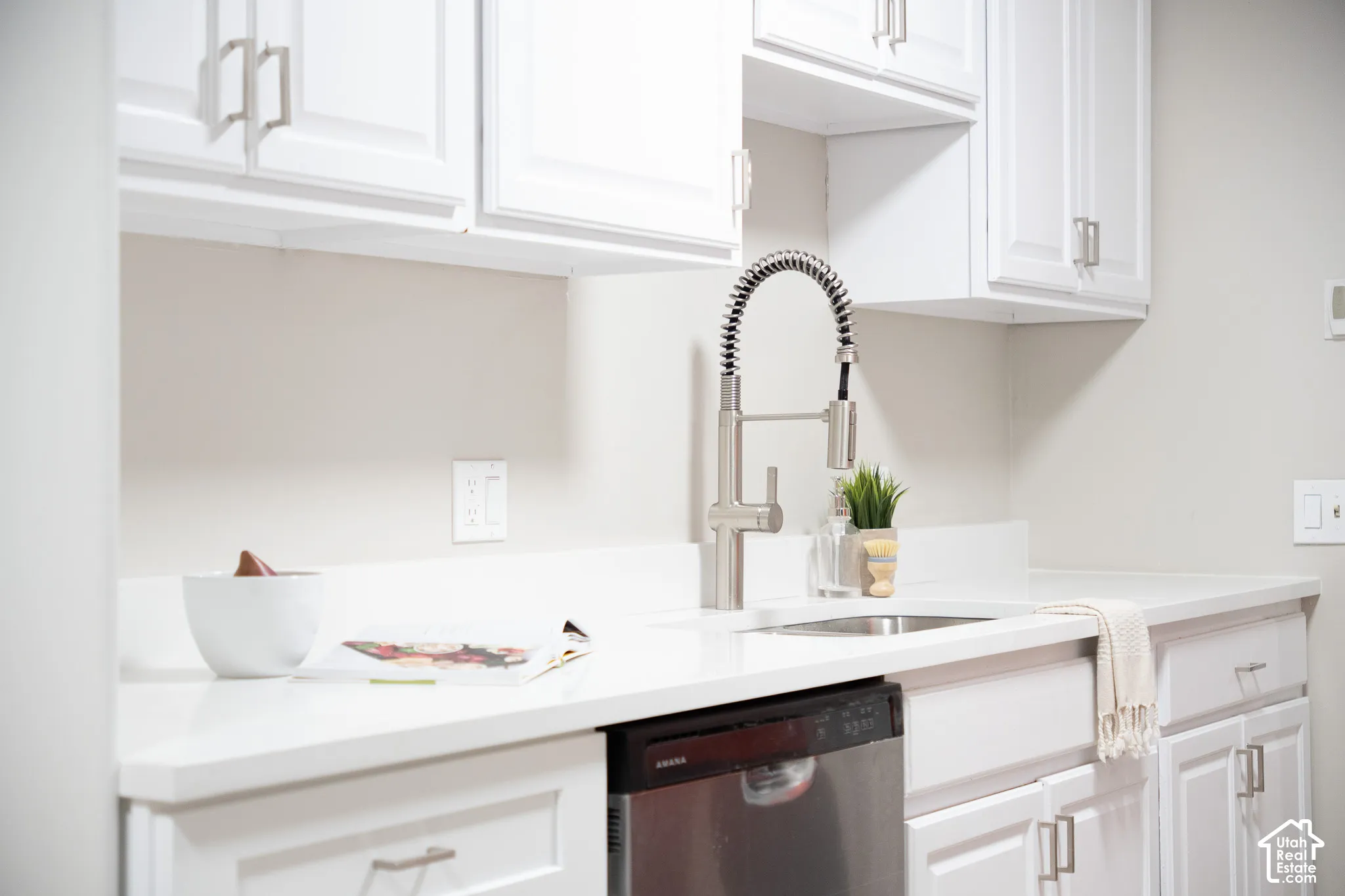 Kitchen featuring white shaker-style cabinetry, solid-surface countertops, a stainless steel undermount sink, a high-arc pull-down faucet, and a stainless steel dishwasher