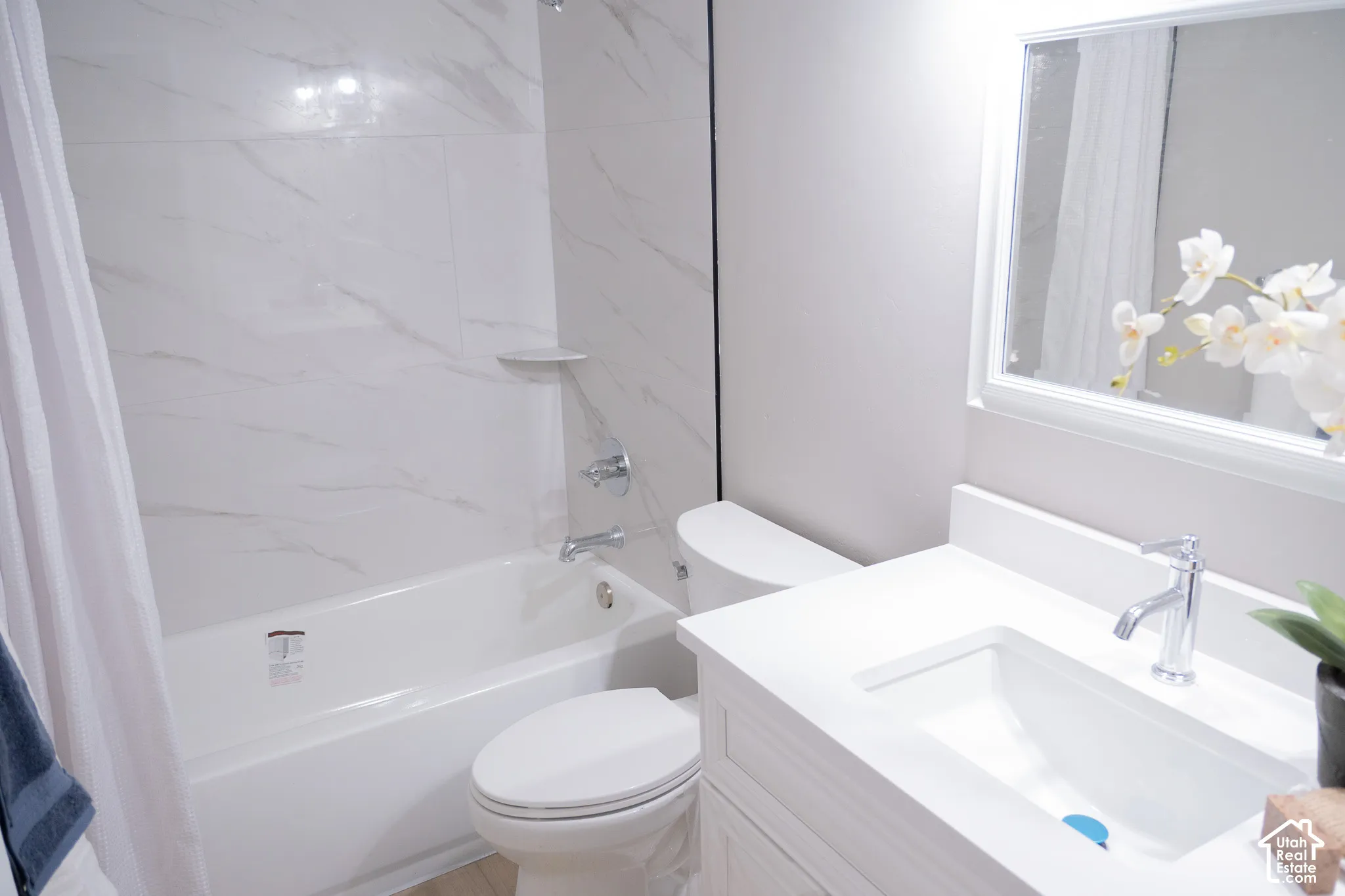 Bathroom featuring a white vanity with a rectangular undermount sink, stone-finish countertop, polished chrome faucet, and a shower-tub combination with full-height stone-finish wall tile