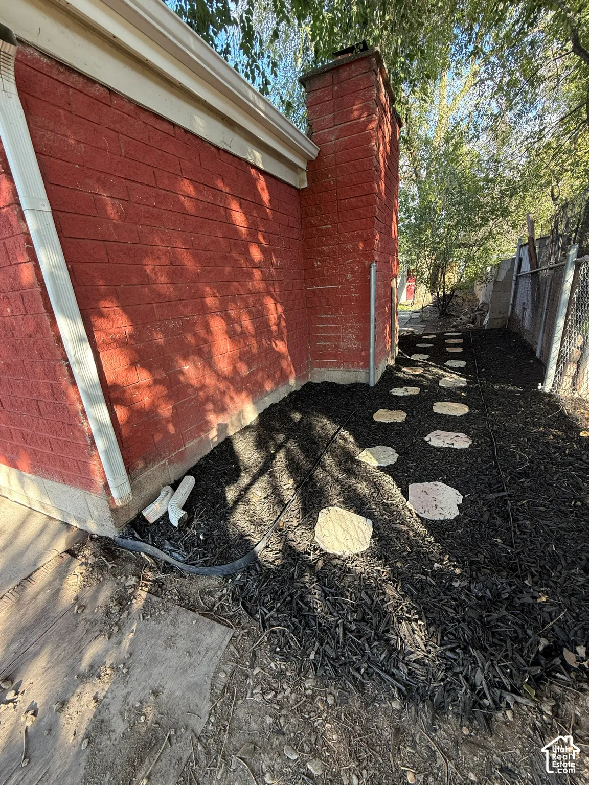 Exterior wall featuring red brick masonry, a prominent brick chimney, and a mulched garden bed with light-toned stone pavers