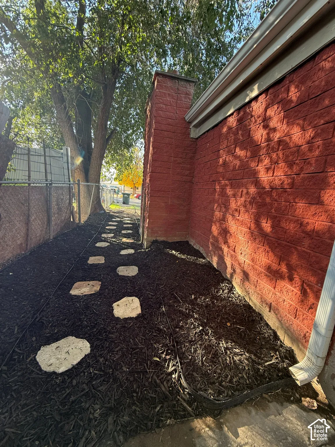 Exterior side yard featuring red brick siding, an integrated masonry chimney, and a stone paver path set in mulch