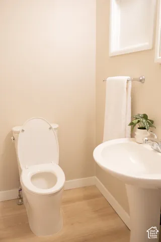 White pedestal sink with chrome faucet, porcelain toilet, wood-finish flooring, and wall-mounted towel bar
