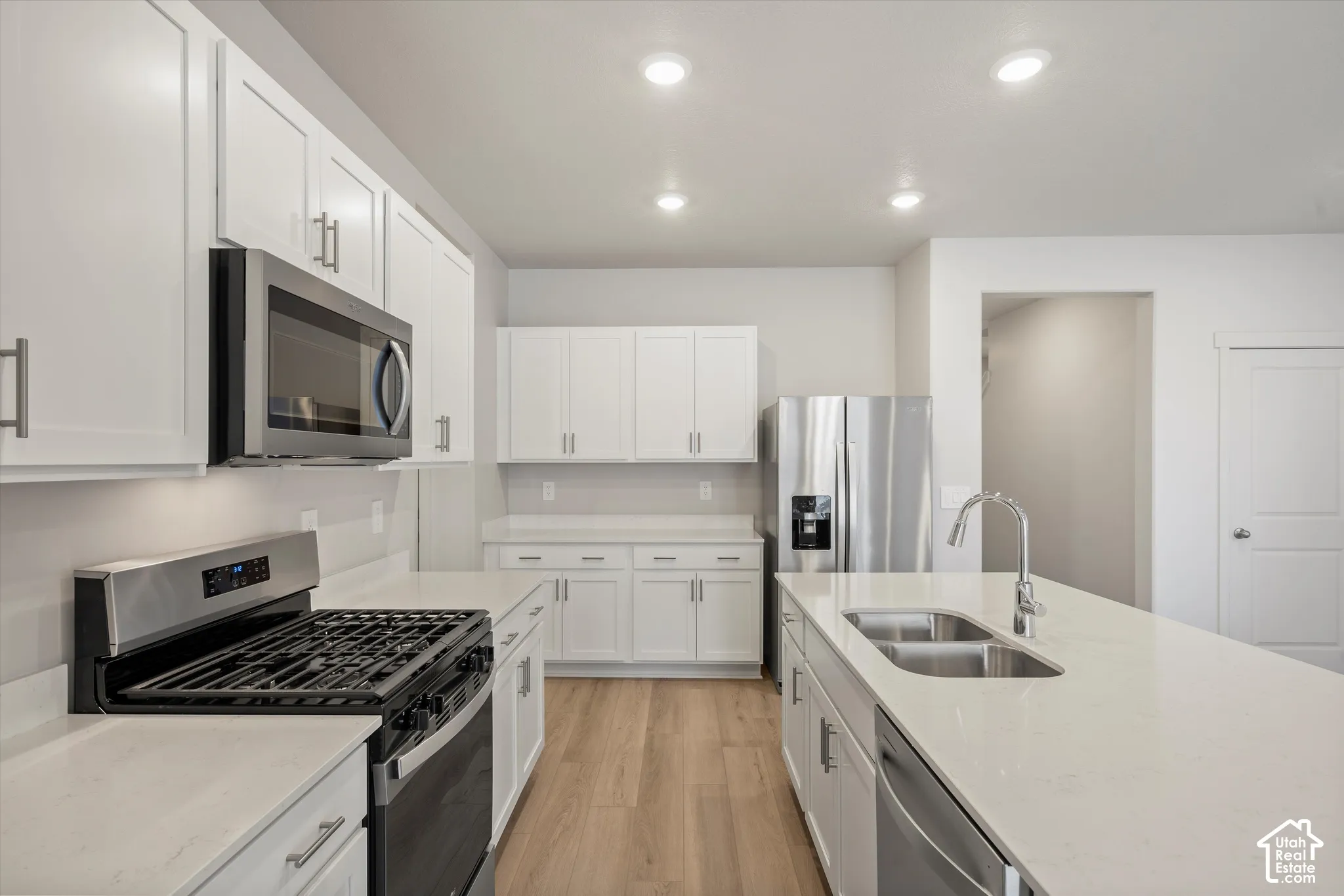**DISCLAIMER** Interior package may vary. Kitchen featuring white shaker-style cabinetry, a quartz countertop island, stainless steel appliances, and wood-finish flooring