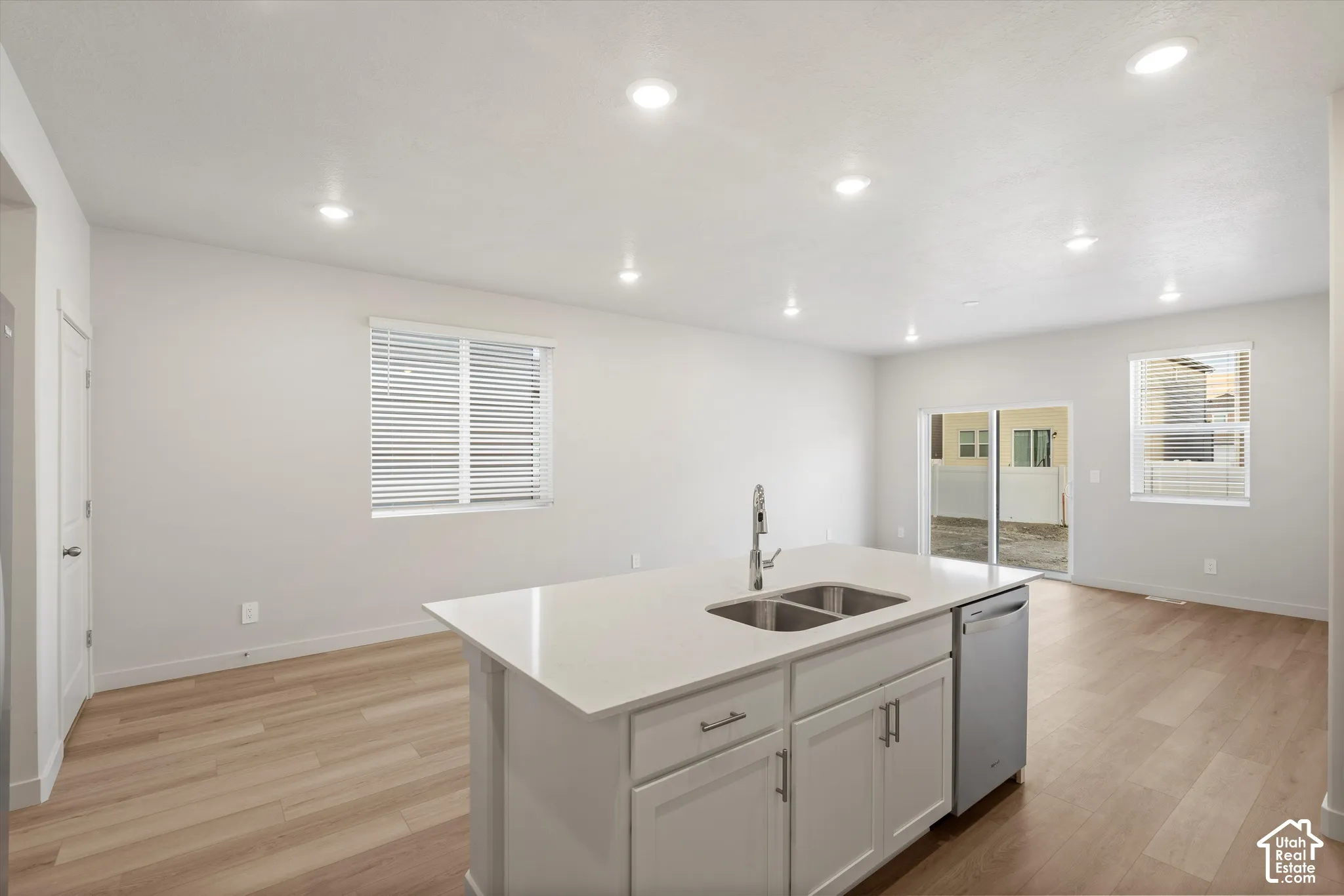 **DISCLAIMER** Interior package may vary. Kitchen featuring an island with a stone-finish countertop, dual-basin stainless steel sink, wood-finish flooring, recessed lighting, and sliding glass door