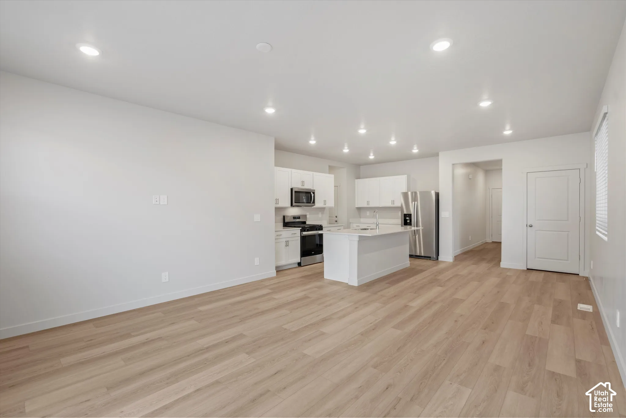 **DISCLAIMER** Interior package may vary. Open-concept interior featuring wood-finish flooring, recessed lighting, white cabinetry, a center kitchen island with quartz countertops, and stainless steel appliances