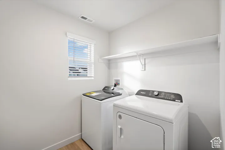 **DISCLAIMER** Interior package may vary. Laundry area featuring wood-finish flooring, a window with horizontal blinds, and built-in wall shelving