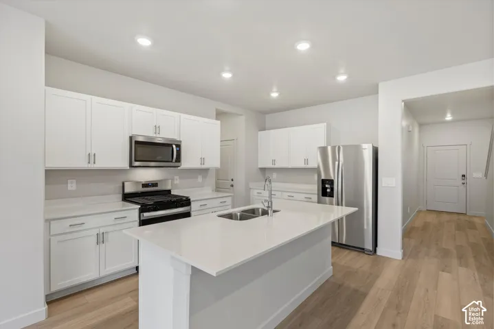 **DISCLAIMER** Interior package may vary. Kitchen featuring white cabinetry, quartz countertops, a central island with a double-basin sink, stainless steel appliances, and wood-finish flooring