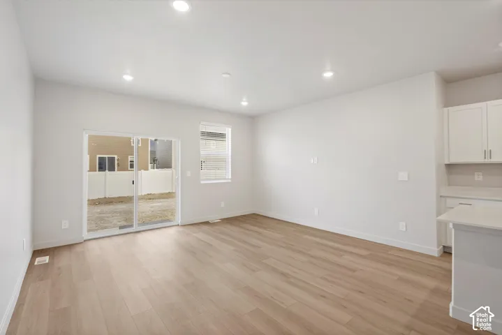 **DISCLAIMER** Interior package may vary. Open-concept interior featuring light wood-finish flooring, recessed lighting, sliding glass door, and white shaker-style cabinetry with solid-surface countertops