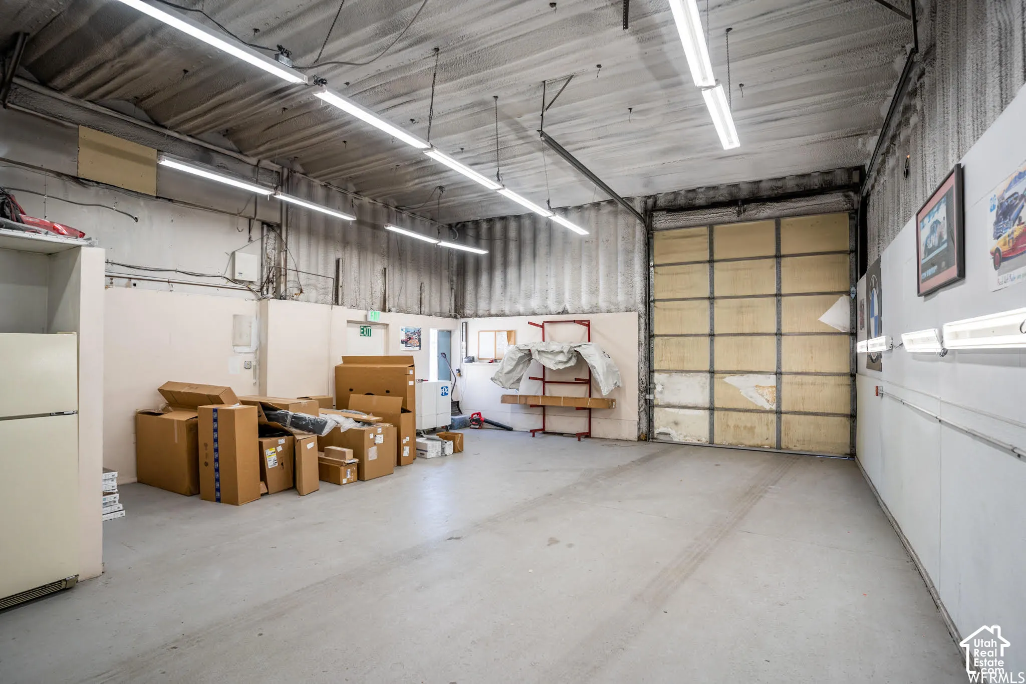 High-ceiling garage space featuring a large roll-up door, corrugated metal walls, and linear fluorescent lighting