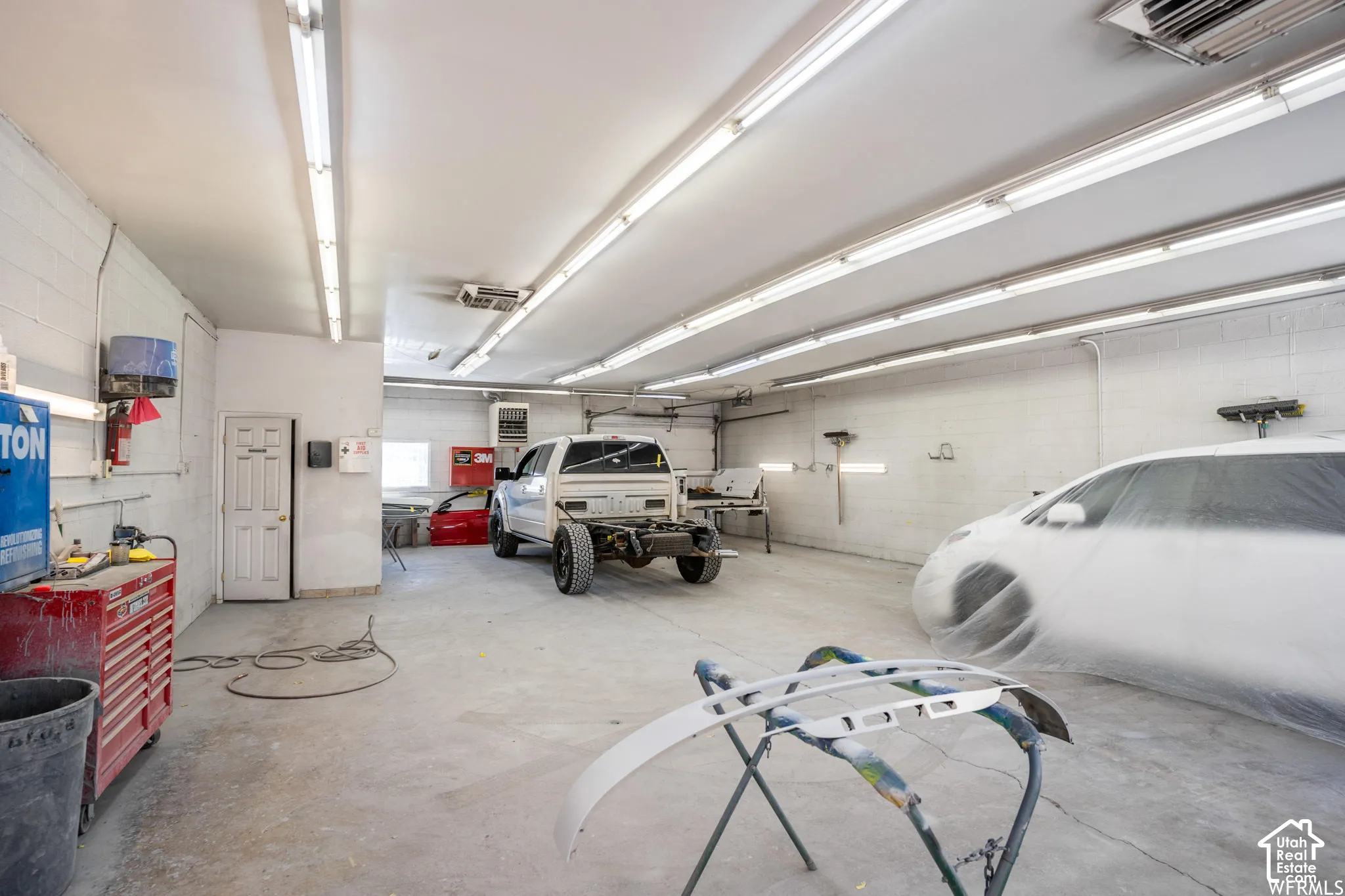 Spacious garage featuring concrete flooring, painted masonry walls, and extensive linear fluorescent overhead lighting