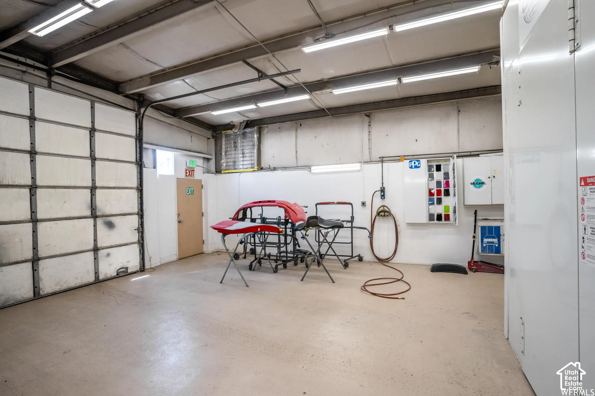High-clearance workspace featuring industrial overhead lighting, finished concrete flooring, a sectional roll-up garage door, and wall-mounted utility cabinetry