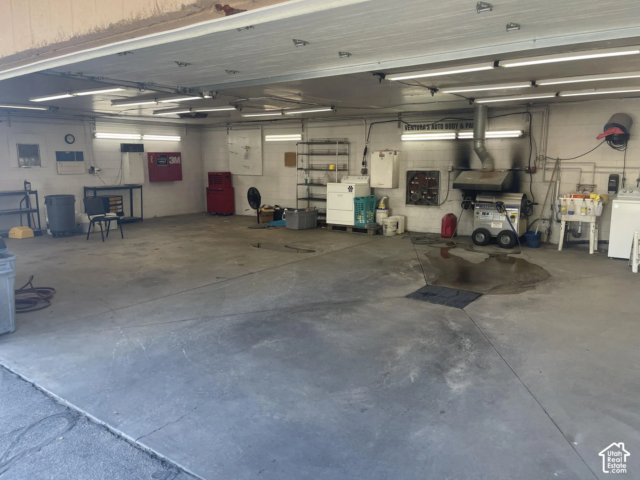 Expansive workshop featuring a concrete floor, high-output overhead lighting, integrated exhaust system, and wall-mounted plumbing utility