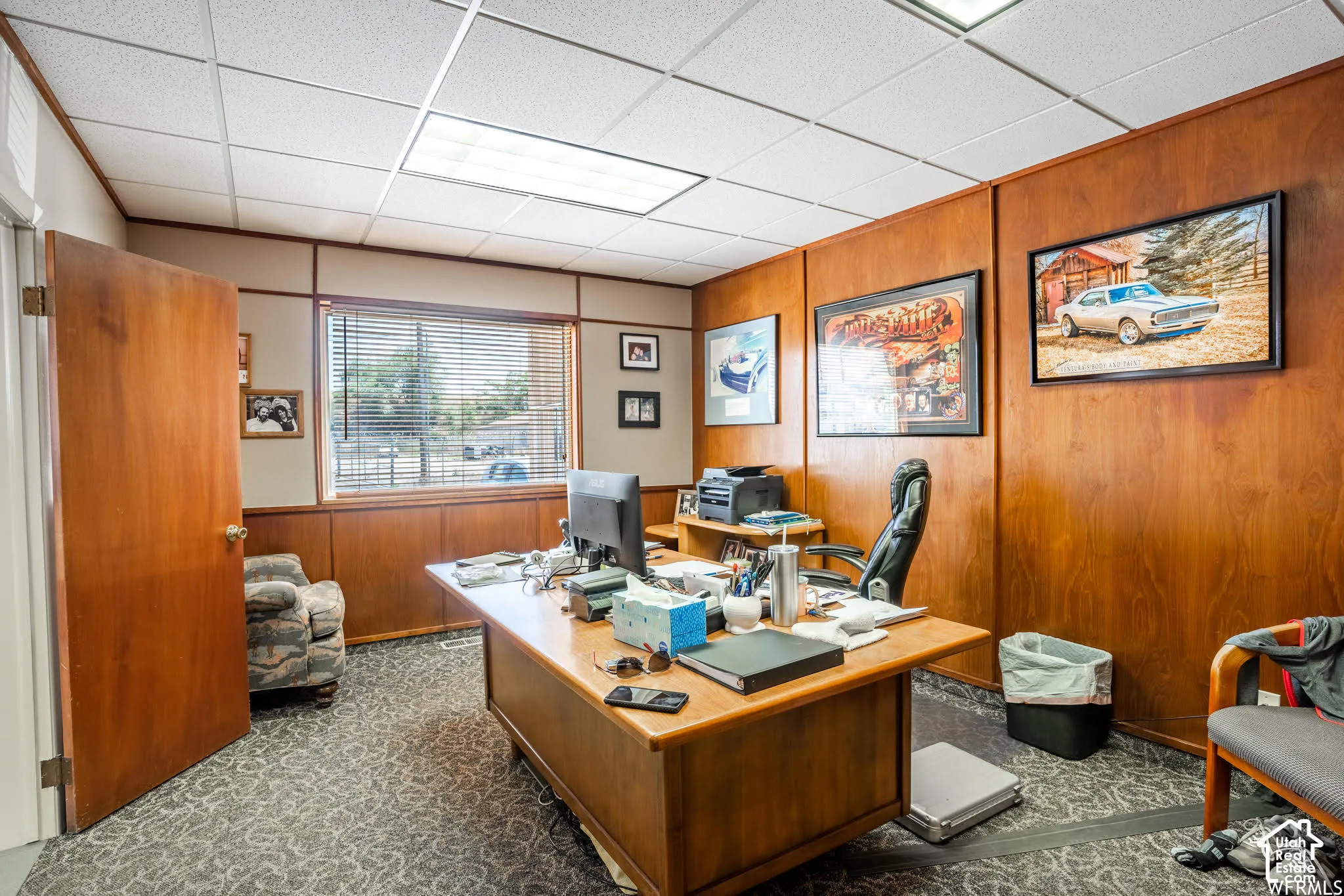 Wood-paneled interior walls, suspended drop ceiling, integrated recessed fluorescent lighting, and window with horizontal blinds