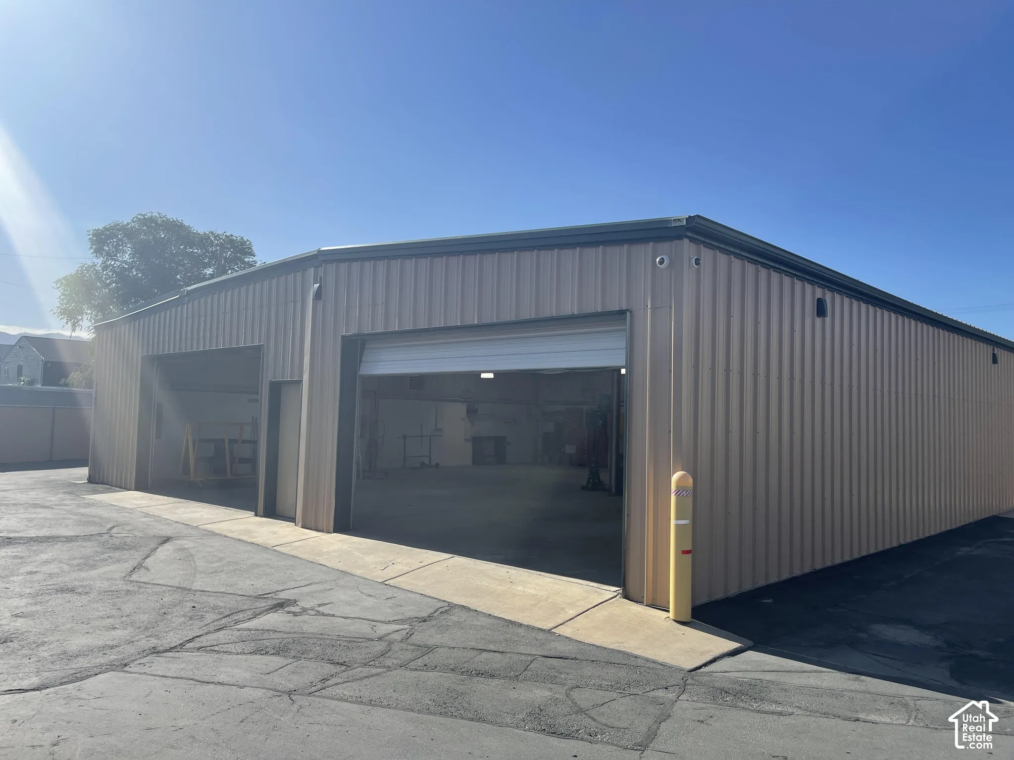 Metal-sided industrial structure featuring two wide-entry roll-up bay doors, expansive concrete flooring, and asphalt exterior paving