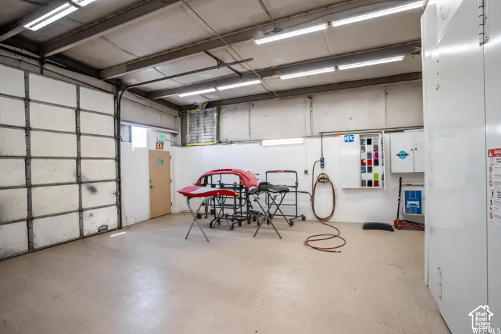 High-clearance workspace featuring industrial overhead lighting, finished concrete flooring, a sectional roll-up garage door, and wall-mounted utility cabinetry