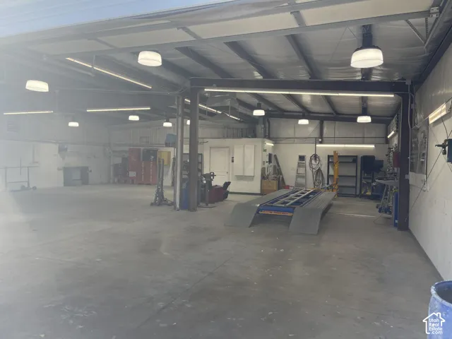 Open-span workspace featuring a concrete floor, high ceilings with exposed structural beams, industrial-style overhead lighting, and an integrated vehicle service ramp